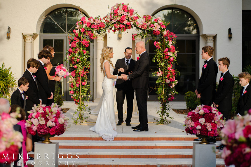 bride and groom exchanging vows in front of floral arch at an outdoor wedding